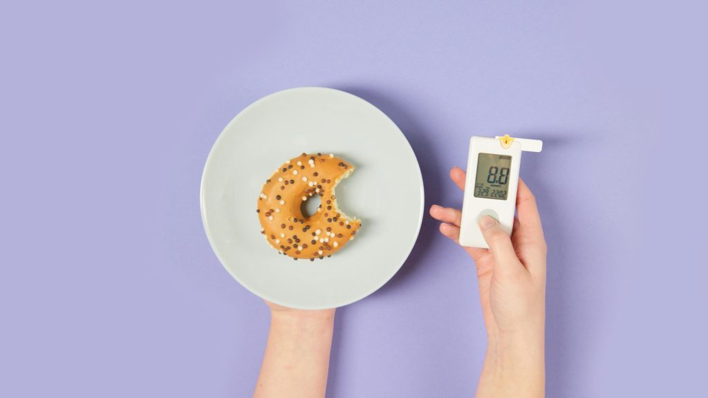 Plato con un donut en una mano y medidor de azúcar en la otra mano
